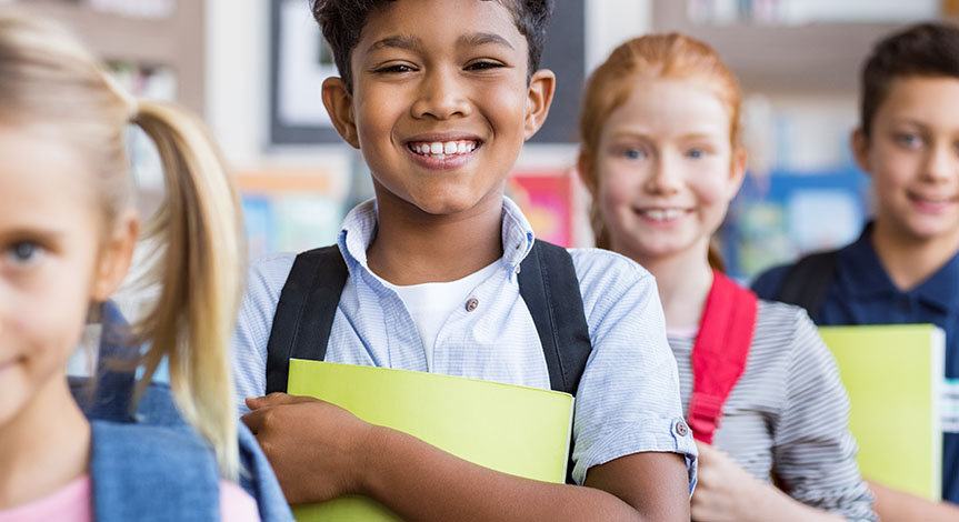 School children standing in a row holding notebooks wearing school bags