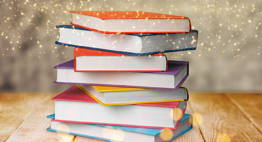 A stack of books on a wood table with gold dust falling from the top